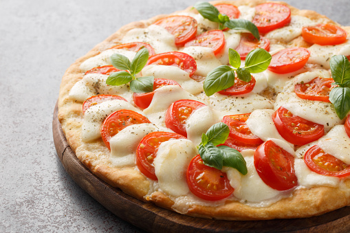 Delicious hot caprese pizza with mozzarella, tomatoes and basil leaves close-up on a wooden board on the table. horizontal
