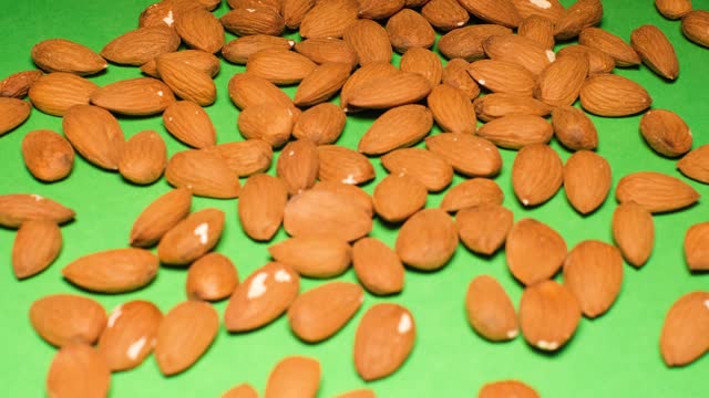 Almond nuts falling on a green background. Almonds are rich in vitamins A and E