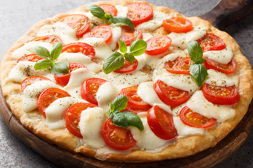 Caprese pizza with melted mozzarella, tomatoes and basil leaves close-up on a wooden board on the table. horizontal