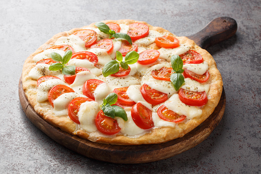 Freshly baked Caprese pizza with cheese, tomatoes and basil close-up on a wooden board on the table. horizontal