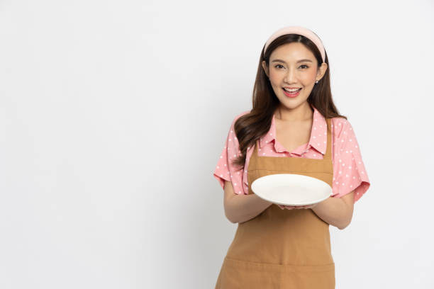 istock Young Asian woman with apron holding empty white plate or dish isolated on white background 1485108381