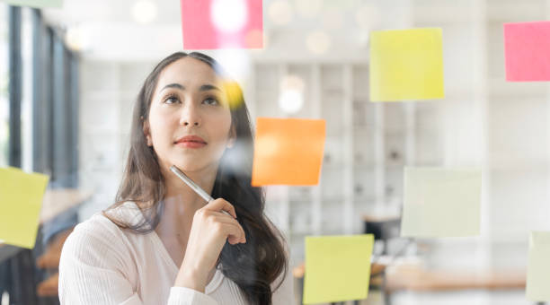 istock Young smiley attractive businesswoman using sticky notes in glass wall to writing strategy business plan to development grow to success 1485108640