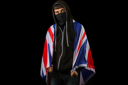 Teenage boy in a hoodie and mask holding a British Flag