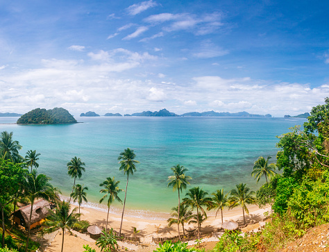 Panorama of a sandy beach and a sea bay with clear wate in El Nido, Palawan island. Blue sky with fluffy clouds in the background.