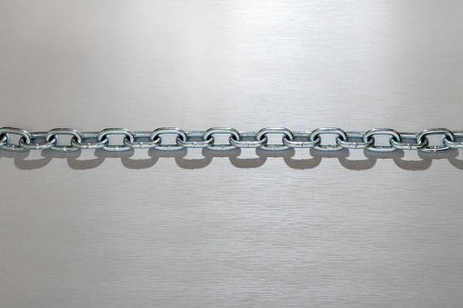 Top view of shiny metal chain with round shaped silver rings and shadow on light gray background