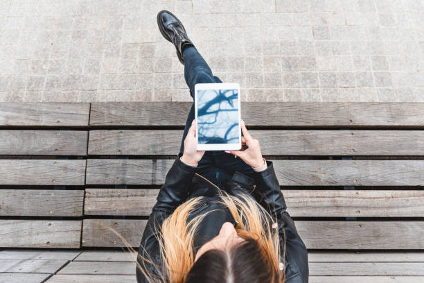 istock Mockup image of woman holding and using white tablet pc with desktop screen while sitting on the wooden bench.Top view.Copy space. 1485118699