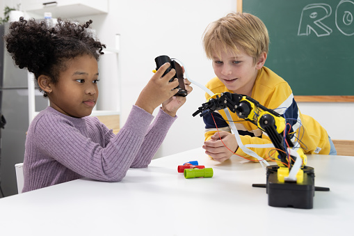 Elementary school students are sitting in the classroom at school and playing to robots class