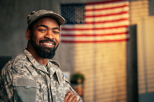 A portrait of a young adult African American army officer inside with the American flag in the background, copy space and looking at camera.