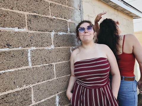 Beautiful plus size body positive and confident Gen Z girl playing around and posing and shopping in downtown Iron Mountain, Michigan in the business district. She is happy and carefree posing among the buildings and ivy growing up the buildings on a city outing day.