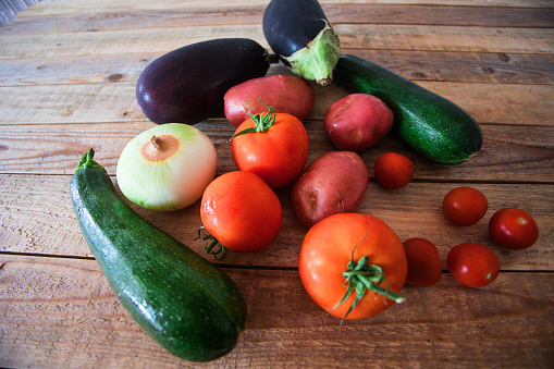 Briam, Greek ratatouille making - fresh ingredients at table, zucchini, eggplant, potato, onion, tomato and cherry tomato, close-up