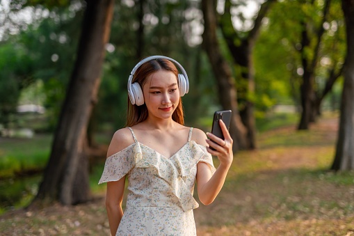 Half body shot of a young asian woman listening to music in a park using phone and simply enjoying her time connecting nature