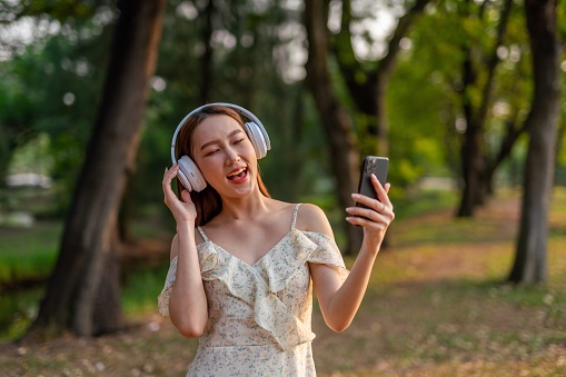 Half body shot of a young asian woman listening to music in a park using phone and simply enjoying her time connecting nature