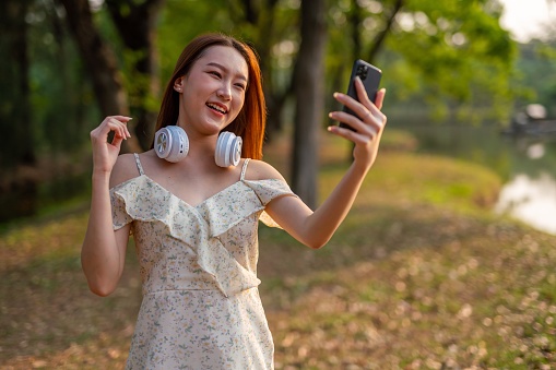 Half body shot of a young asian woman listening to music in a park using phone and simply enjoying her time connecting nature