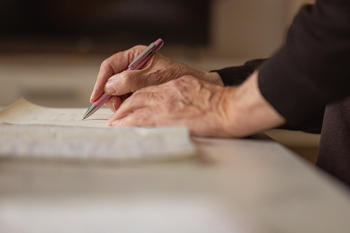 Close up shot of a senior man hands, writing in his old notebook.