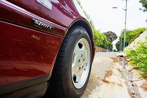 Cape Town, South Africa - February 5, 2023: Low angle view of the front wheel of a well-preserved late-1990s Mercedes-Benz 230K Sport in deep metallic maroon, parked in a street in a wealthy suburb of Cape Town, South Africa.