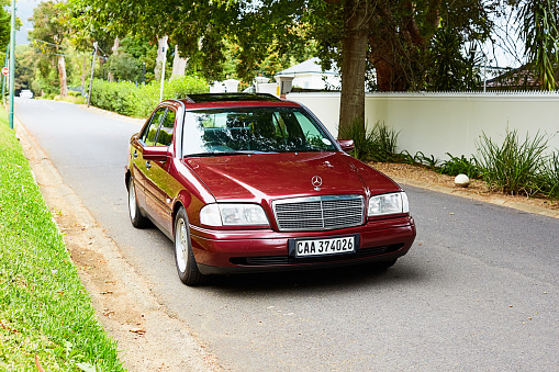 Cape Town, South Africa - February 5, 2023: A well-preserved late-1990s Mercedes-Benz 230K Sport in deep metallic maroon, parked in a street in a wealthy suburb of Cape Town, South Africa.