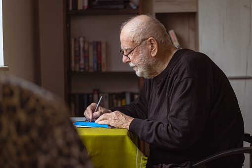 An older man with Alzheimer's Disease is writing his favorite memories in a journal.