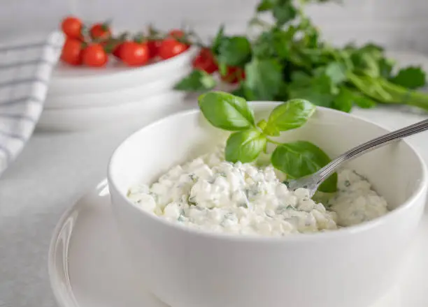 Healthy vegetarian protein snack with a marinated cottage cheese, herb salad. Served ready to eat in a white bowl with fork on white kitchen counter background. Suitable for fitness, diet and healthy eating.