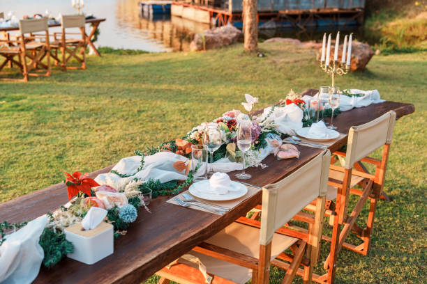Rustic style wooden dining long table with flower, wine glass, candle decoration at dinner by the river in the sunset