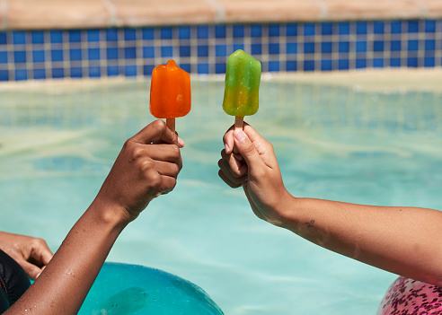 Close up of friends holding ice lolly popsicles in the swimming pool, beat heat. High quality photo