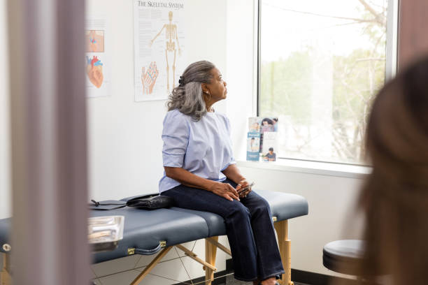 female patient sits on the exam table and gazes out the window - telephone doctor medical exam healthcare and medicine imagens e fotografias de stock