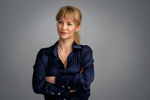 Close-up of an attractive middle aged woman smiling and looking away. Blond haired female wearing casual clothes while standing at isolated background. Copy space. Studio shot.