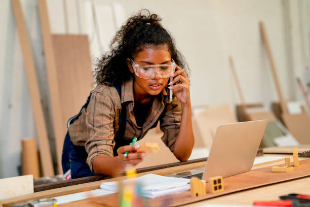 istock Carpenter woman use mobile phone to contact customer and write the discussion data to notebook about wood product in front of laptop in workplace. 1485138714