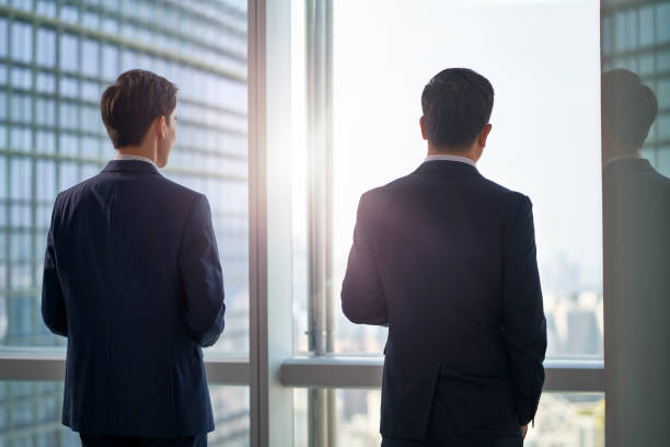 istock two asian businessmen standing by the window talking chatting 1485138795