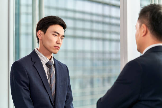 istock two asian business men standing and talking by the window in office 1485138872