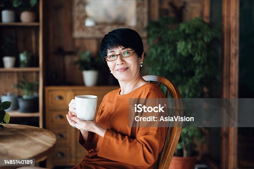 istock Portrait of senior Asian woman enjoying a cup of coffee, sitting at dining table against green plants, relaxing at home. Elderly and retirement lifestyle 1485140189