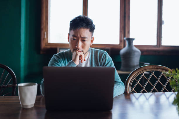 istock Contemplating young Asian man working on laptop, concentrated on work. Looking stressed out and worried while working at home. Business challenges. Managing personal finance. Meeting deadlines. Freelancer, small business and self-employment concept 1485140370