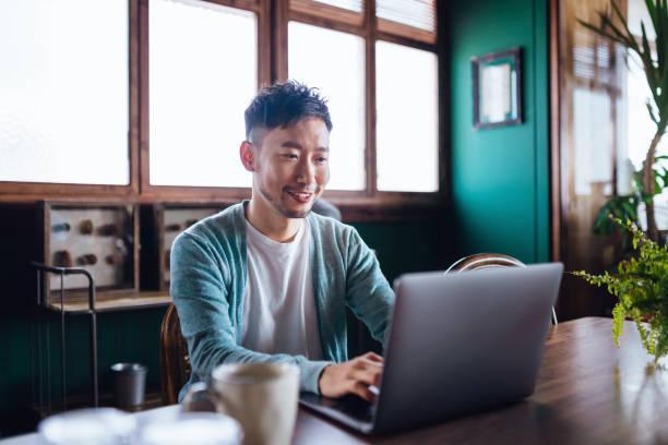 istock Young Asian man working from home, using laptop computer in home office. Remote working, freelancer, small business, self-employment concept 1485140429