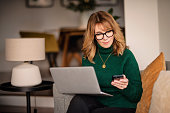 istock Blond haired mature woman using notebook and text message while sitting at home 1485140585
