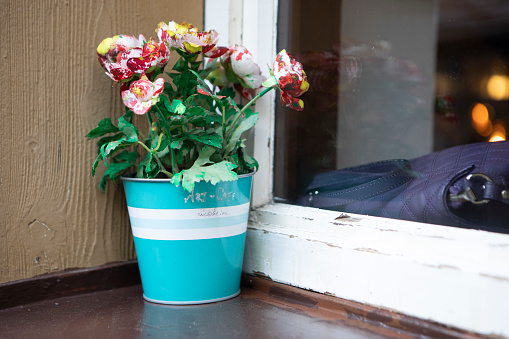 Turquoise-coloured metal pot with artificial flowers outside a window