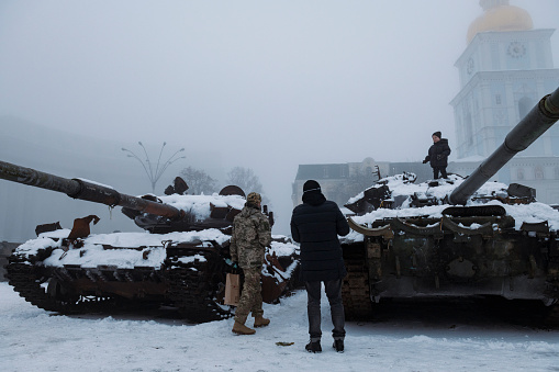 Kyiv, Ukraine - December 8, 2022: Two men stand nearby as a child plays on a damaged, captured Russian tank that has been put on display outside St. Michael's Golden-Domed Monastery in central Kyiv.
