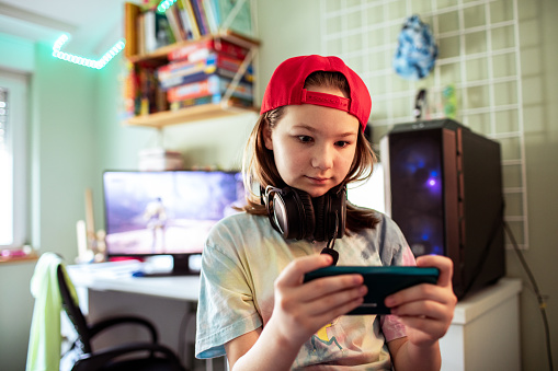 Close up of a Young girl playing games on her smart phone in her bedroom by the desktop computer