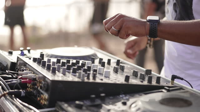 DJ handling controller close up with hands moving outdoors in the day light at sunset near the beach wearing bracelets and a smart watch