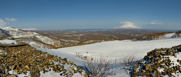 Russia. Far East, Kuril Islands. View of the snow-covered volcanoes of Iturup Island, overgrown with larch and gnarled stone birch.