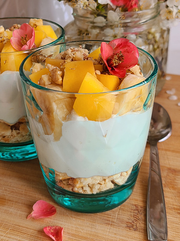 Tropical mango and pineapple parfaits in mason jars, scene on dark rustic background