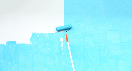 Paint roller with blue paint on old wall