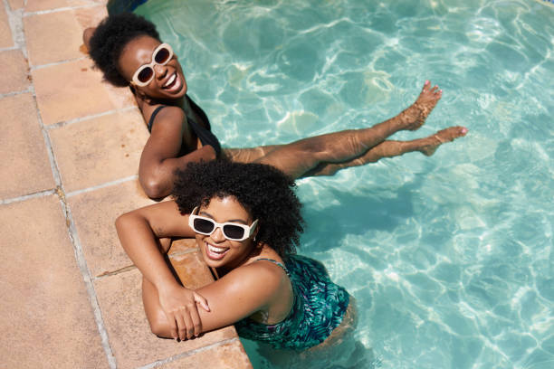 Two beautiful Black women cool off in swimming pool, summer heatwave