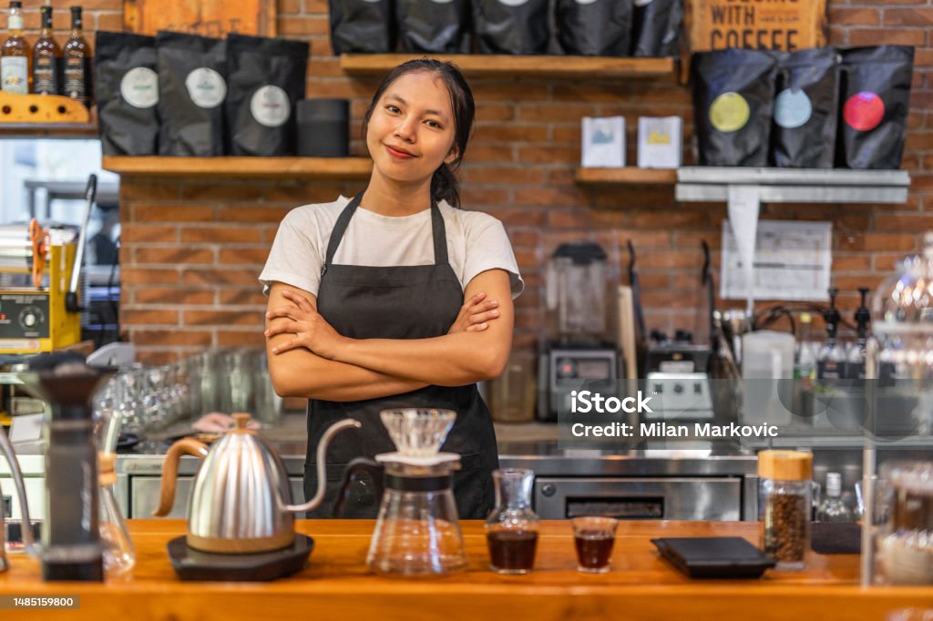 A smiling young Indonesian woman prepares coffee in a cafe in a traditional way Smiling young Indonesian woman preparing coffee in cafe in traditional way, location Bali, ideal place for vacation 18-19 Years Stock Photo