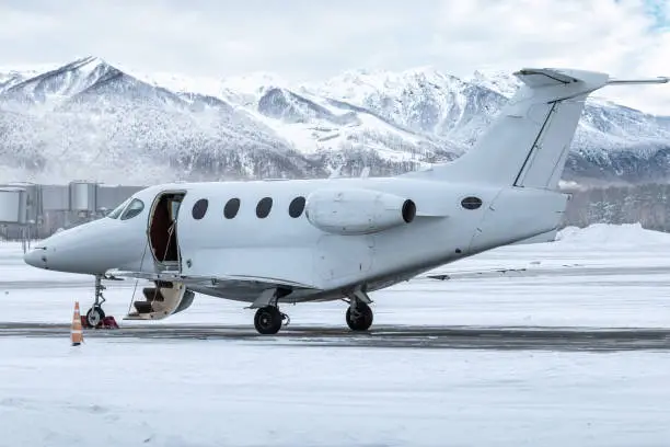 Modern white business jet with an opened gangway door at the winter airport apron on the background of high scenic snow capped mountains