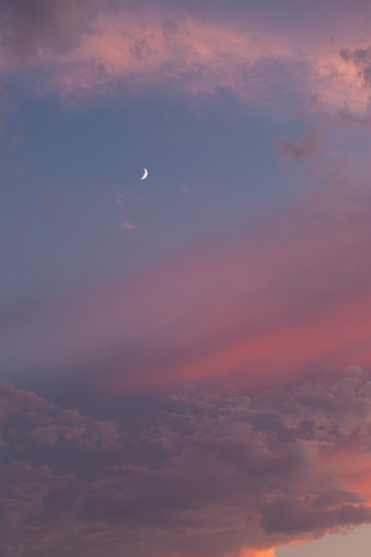 The quarter moon is visible in the blue sky. The clouds are pink to orange-grey.