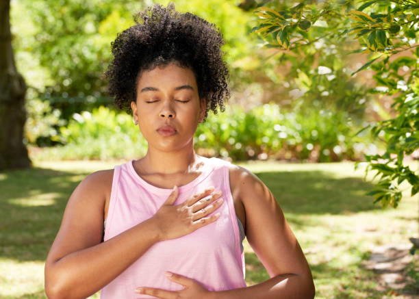 Young mutli-ethnic woman practices deep belly breathing, meditation in park stock photo