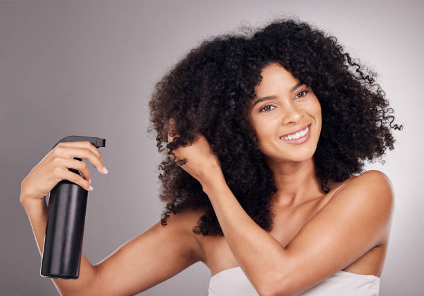 Face of black woman spray product on hair for natural wellness, growth and shine on gray background. Beauty, luxury salon and happy girl smile with hairspray, cosmetic products and keratin treatment cara de la mujer negra producto en aerosol sobre el cabello para el bienestar natural, el crecimiento y el brillo sobre fondo gris. belleza, salón de lujo y sonrisa de chica feliz con laca para el cabello, productos cosméticos y tratamiento de keratina