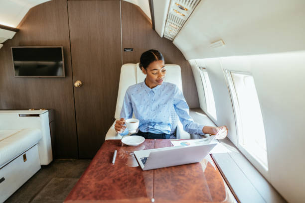 giovane donna d'affari africana che vola con l'aereo privato e utilizza il computer portatile per lavoro - commercial airplane finance airplane private airplane foto e immagini stock
