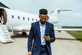 African American entrepreneur traveling by private jet, and using smart phone before boarding