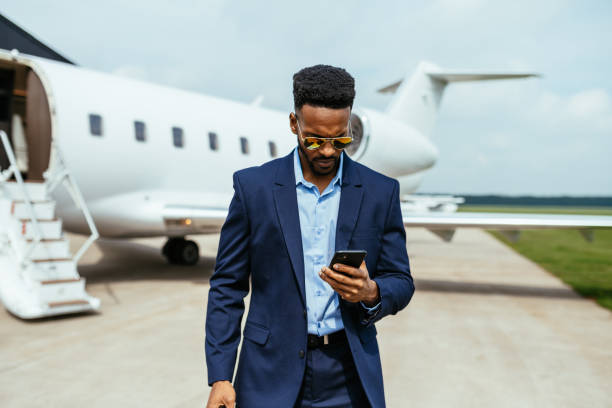 African American entrepreneur traveling by private jet, and using smart phone before boarding stock photo