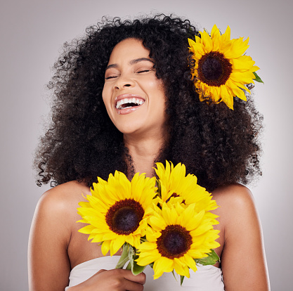 Portrait, cheerful or face of black woman with sunflower in hair in studio for spring time, luxury spa or self care. Aesthetic, happy model or girl model with plant for skincare, cosmetic or makeup